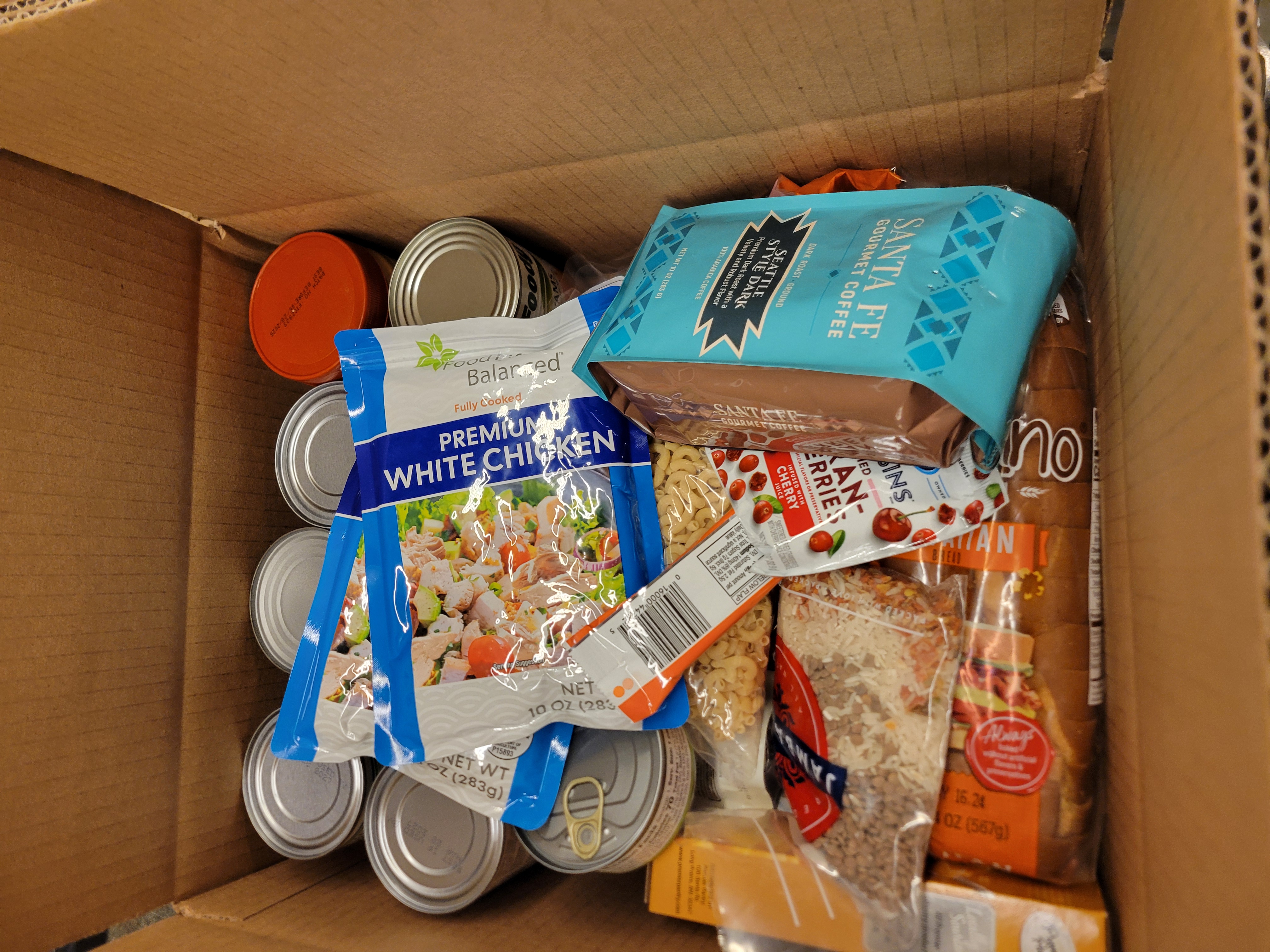 Box full of canned goods, bread, pouches of chicken, and other dry goods.